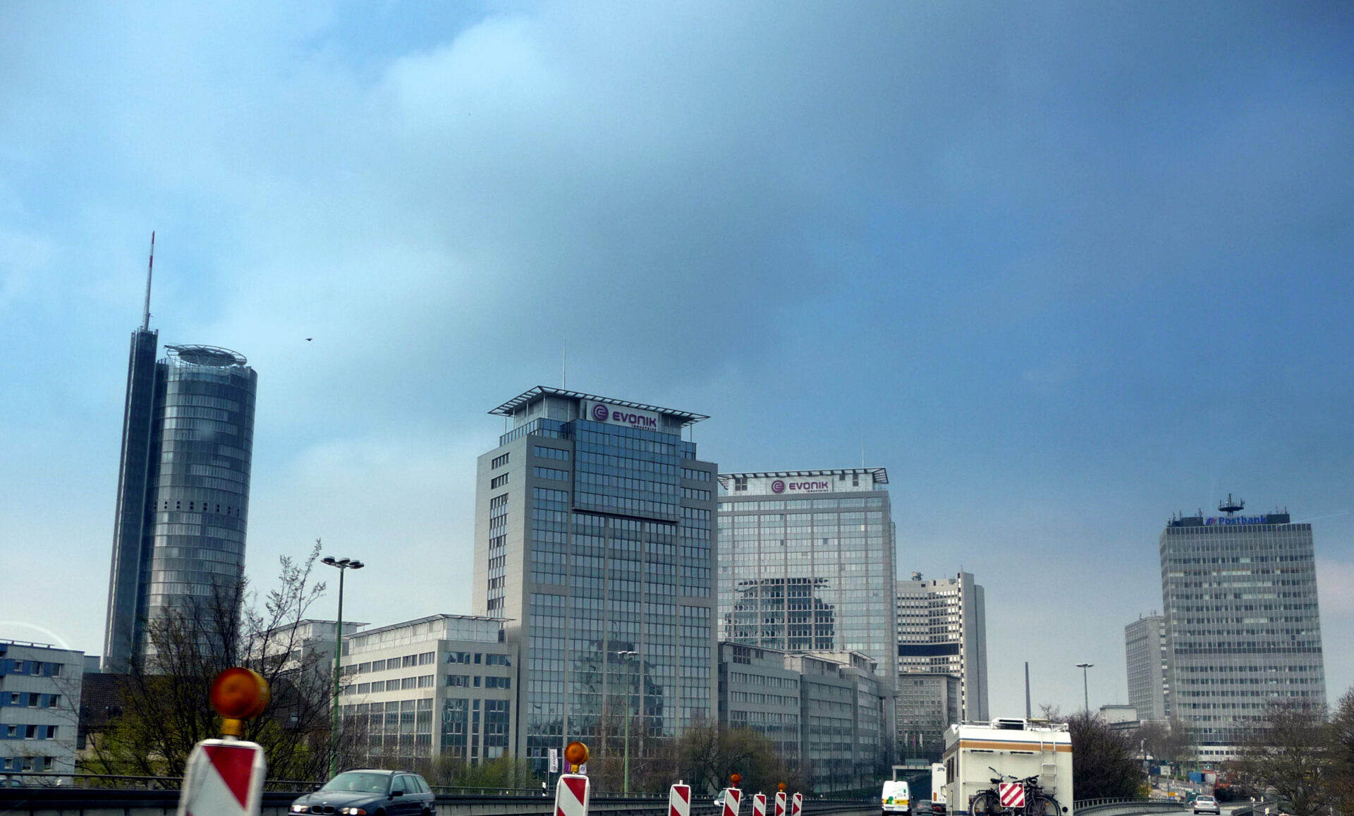Blick auf die Skyline von Essen mit markanten Hochhäusern wie dem RWE-Turm und dem Postbank-Hochhaus, fotografiert aus der Perspektive der Autobahn A40 im Vordergrund bei Tageslicht.